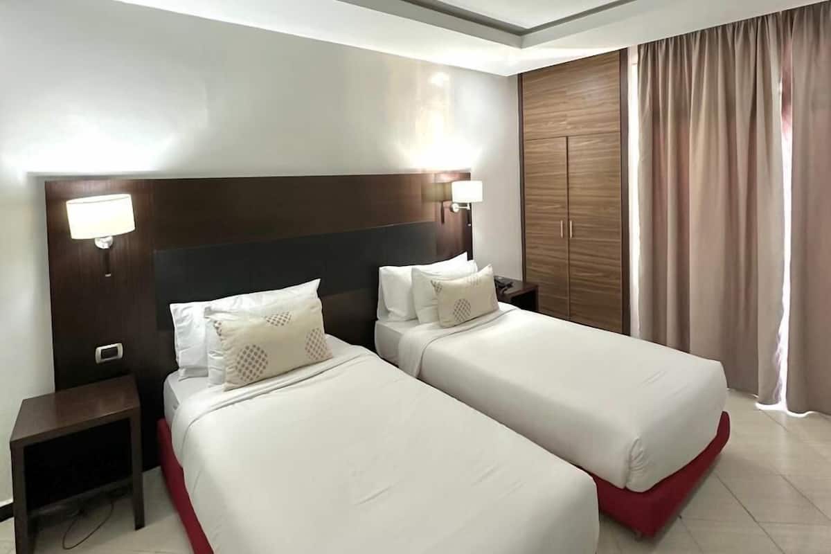Ein Hotelzimmer mit zwei Betten, einem Nachttisch, einem Holz-Kopfteil, einer Lampe und einem Kleiderschrank.