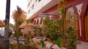 Un hôtel à la façade rouge, doté d’un espace extérieur aménagé avec des parasols et des plantes en pot.