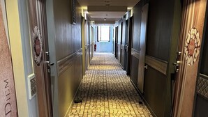 Un pasillo de hotel con suelo de piedra, puertas con números decorativos y un extintor en la pared.