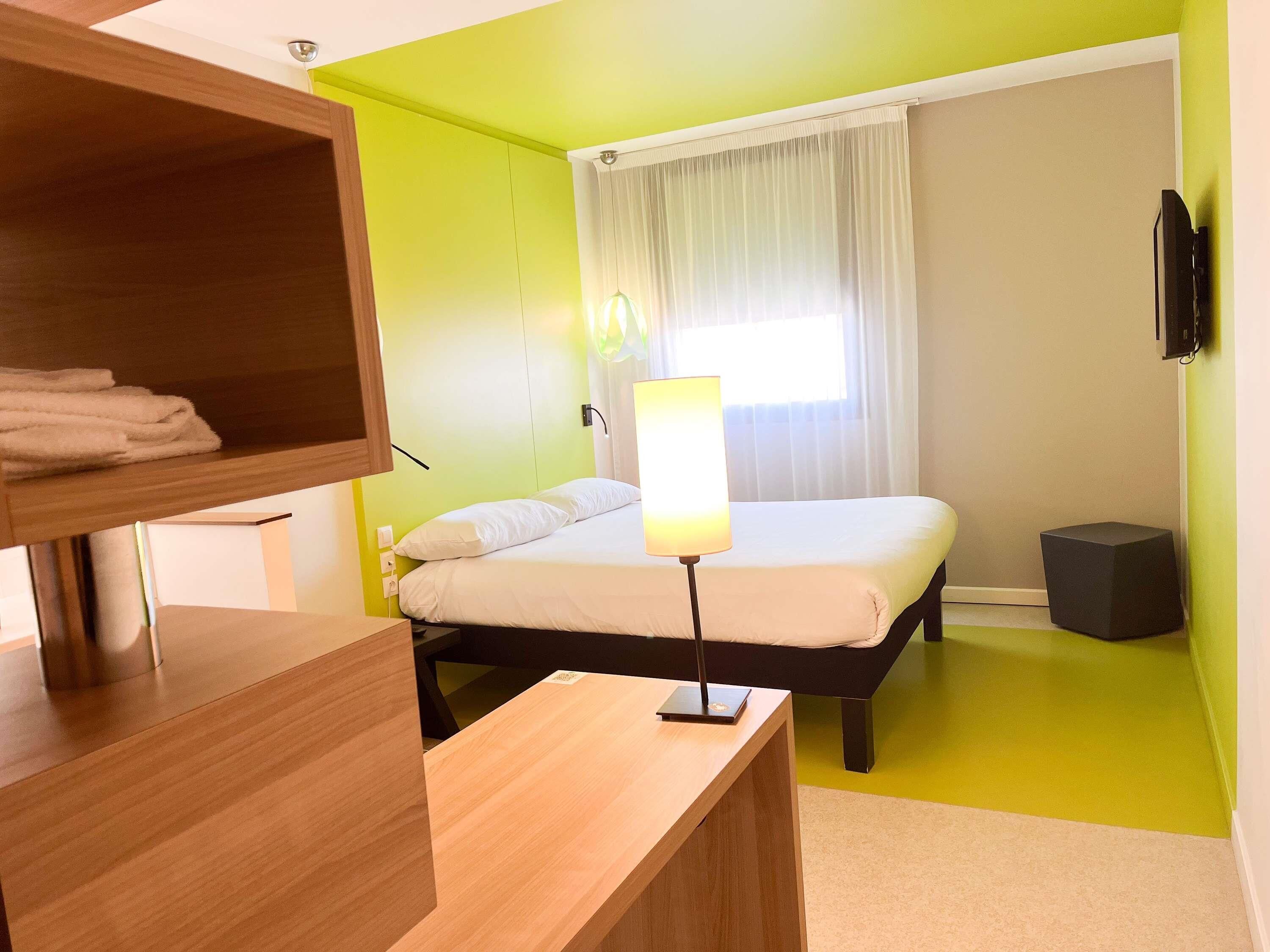 A hotel room with a bed, a bedside lamp, a TV, and a wooden desk.