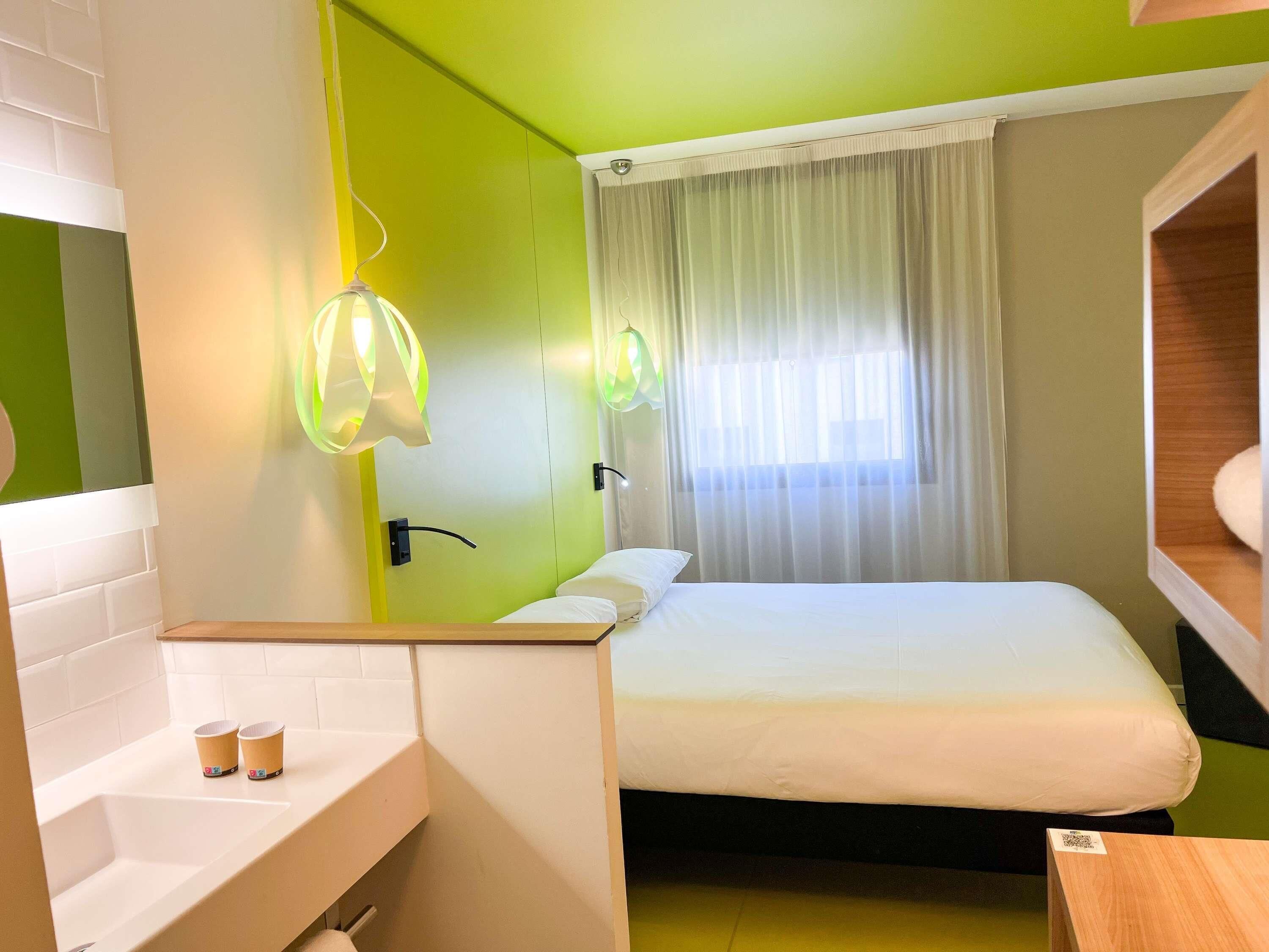 Habitación de hotel con cama, baño con lavamanos y dos tazas, espejo y ventana con cortinas.