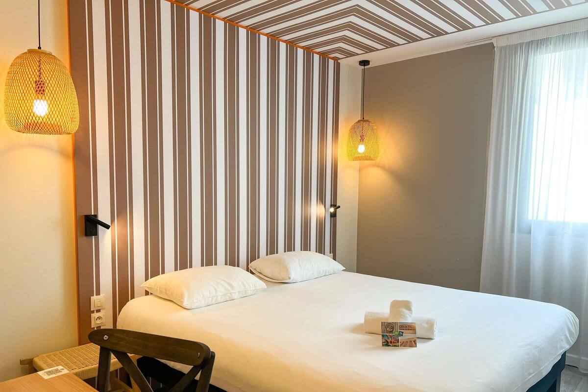 A hotel room with a bed, a chair, a table, and a striped wall.