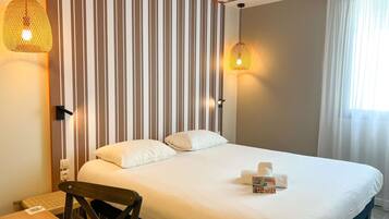 Habitación de hotel con cama, una silla, una mesa y una pared a rayas.