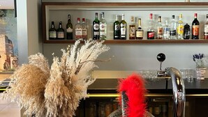 Zona de bar con diversas botellas de licores, un arreglo decorativo de plumas y un grifo.