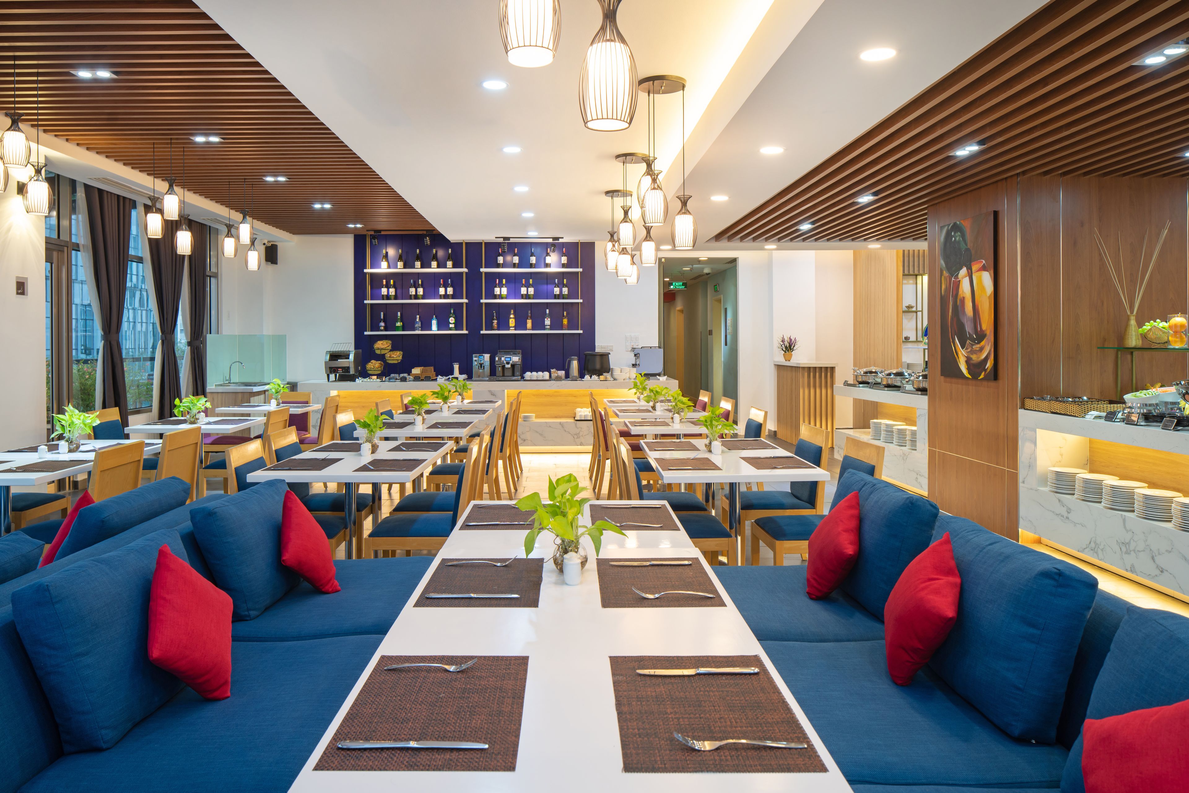 A modern restaurant with blue sofas, dining tables, and a bar area.