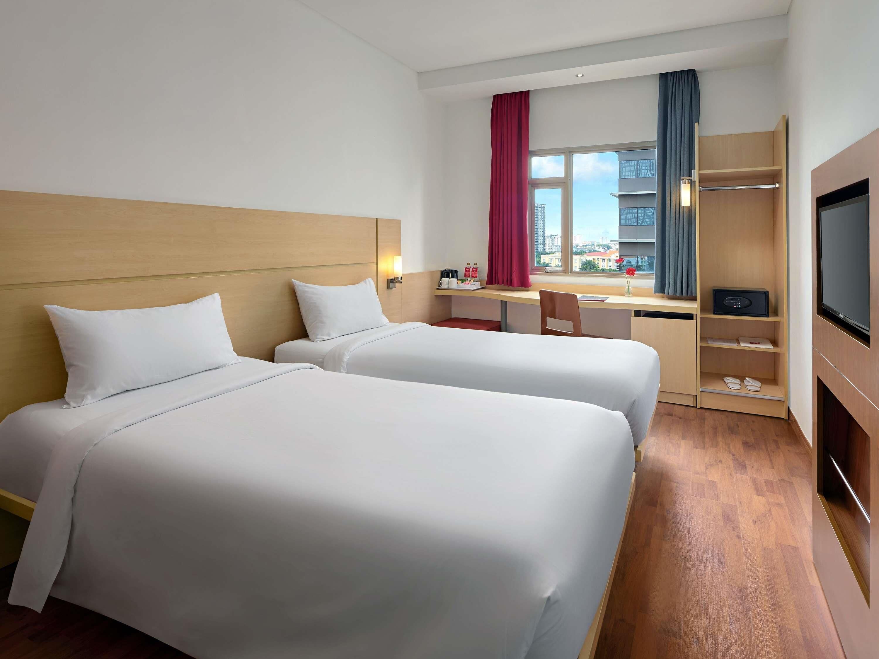 Ein Hotelzimmer mit zwei Betten, einem Schreibtisch, einem Fernseher und Blick auf die Stadt.