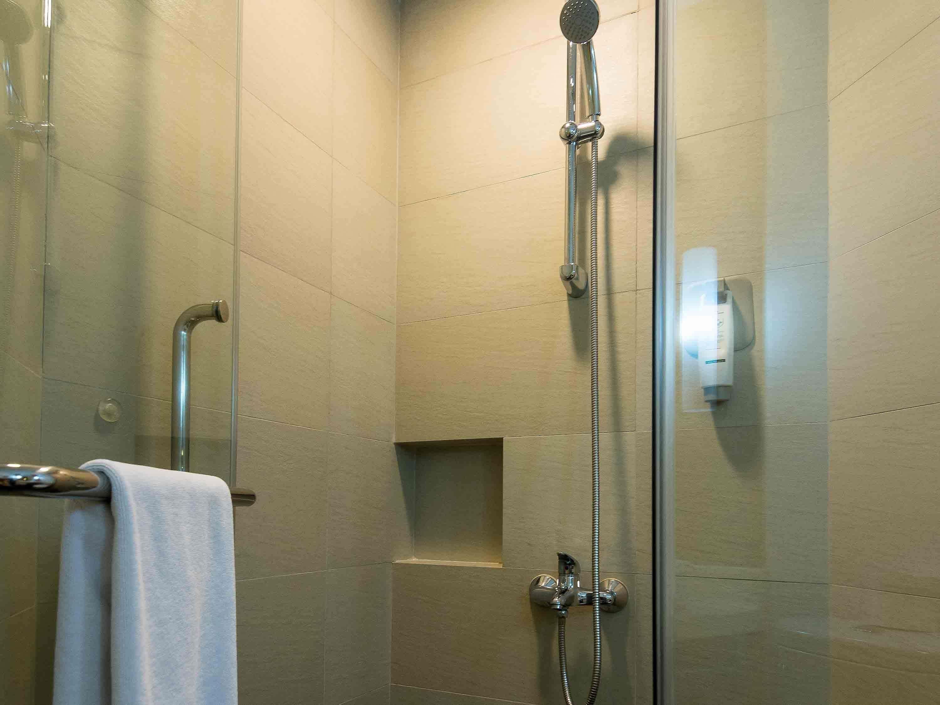 A glass-enclosed shower with a handheld showerhead and a wall-mounted faucet.