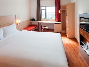 A hotel room with a large bed, a desk, a chair, a TV, and a window with curtains. - ibis Saigon South (Ho Chi Minh City)