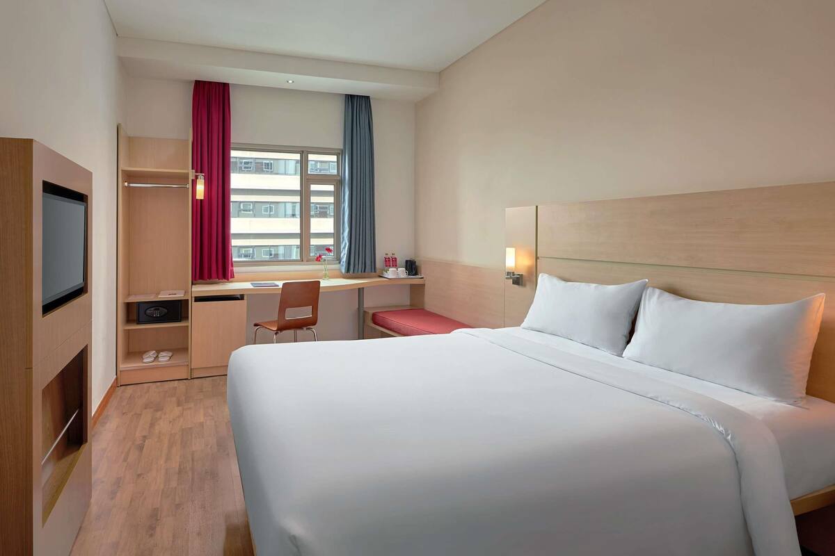 Een hotelkamer met een groot bed, een bureau met stoel, een televisie en een raam met gordijnen.