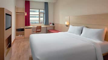 Quarto de hotel com uma cama grande, uma escrivaninha com cadeira, televisão e janela com cortinas.