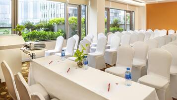 A conference room with white chairs, a long table, and large windows with a view of buildings and greenery.