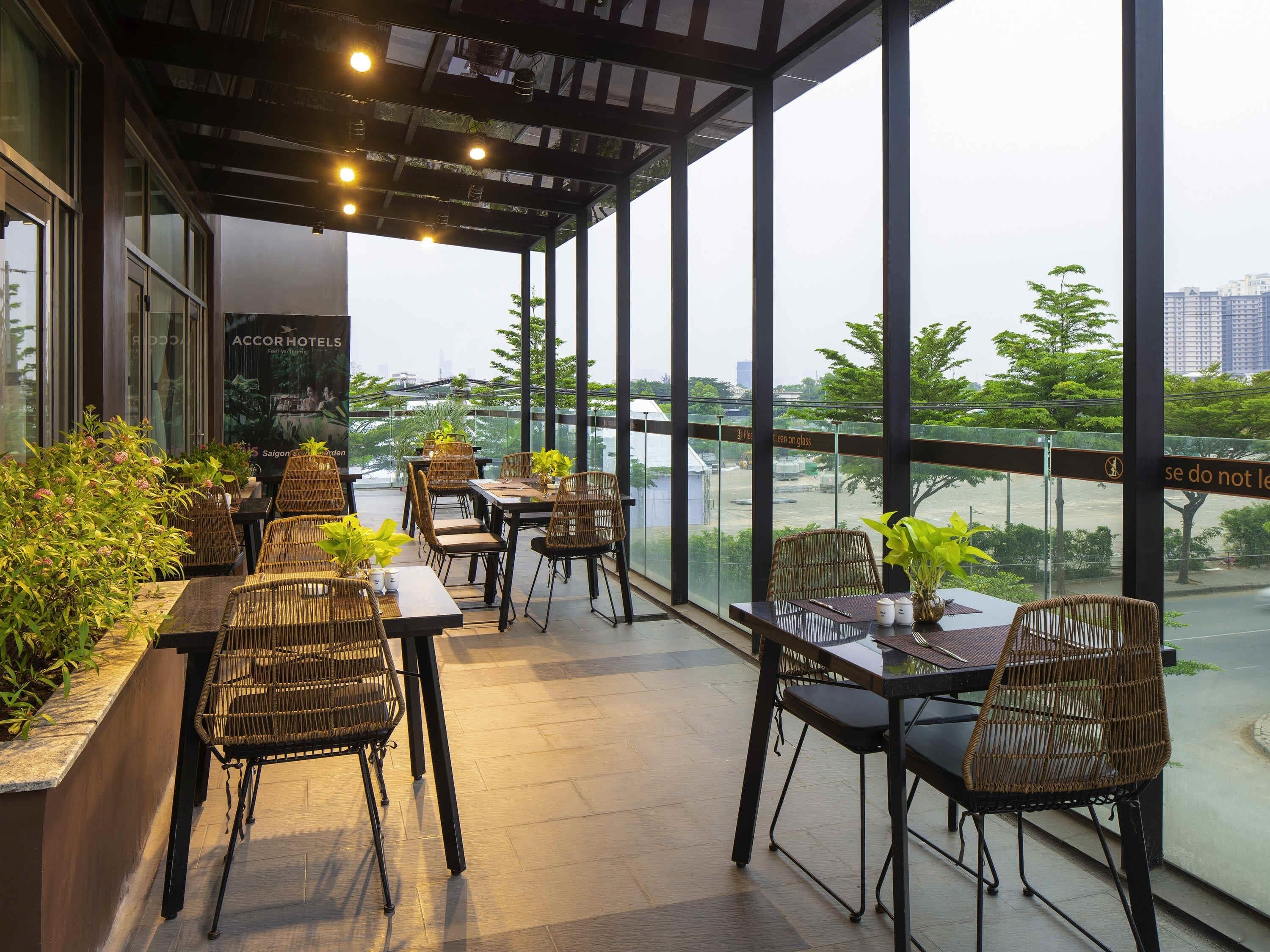 Un restaurante con terraza, grandes ventanales y plantas en macetas.