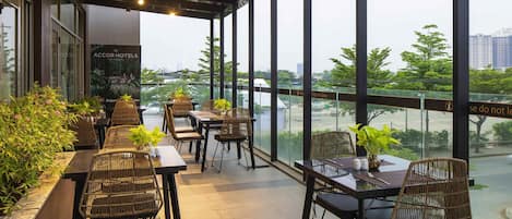 A restaurant with outdoor seating, large windows, and potted plants.