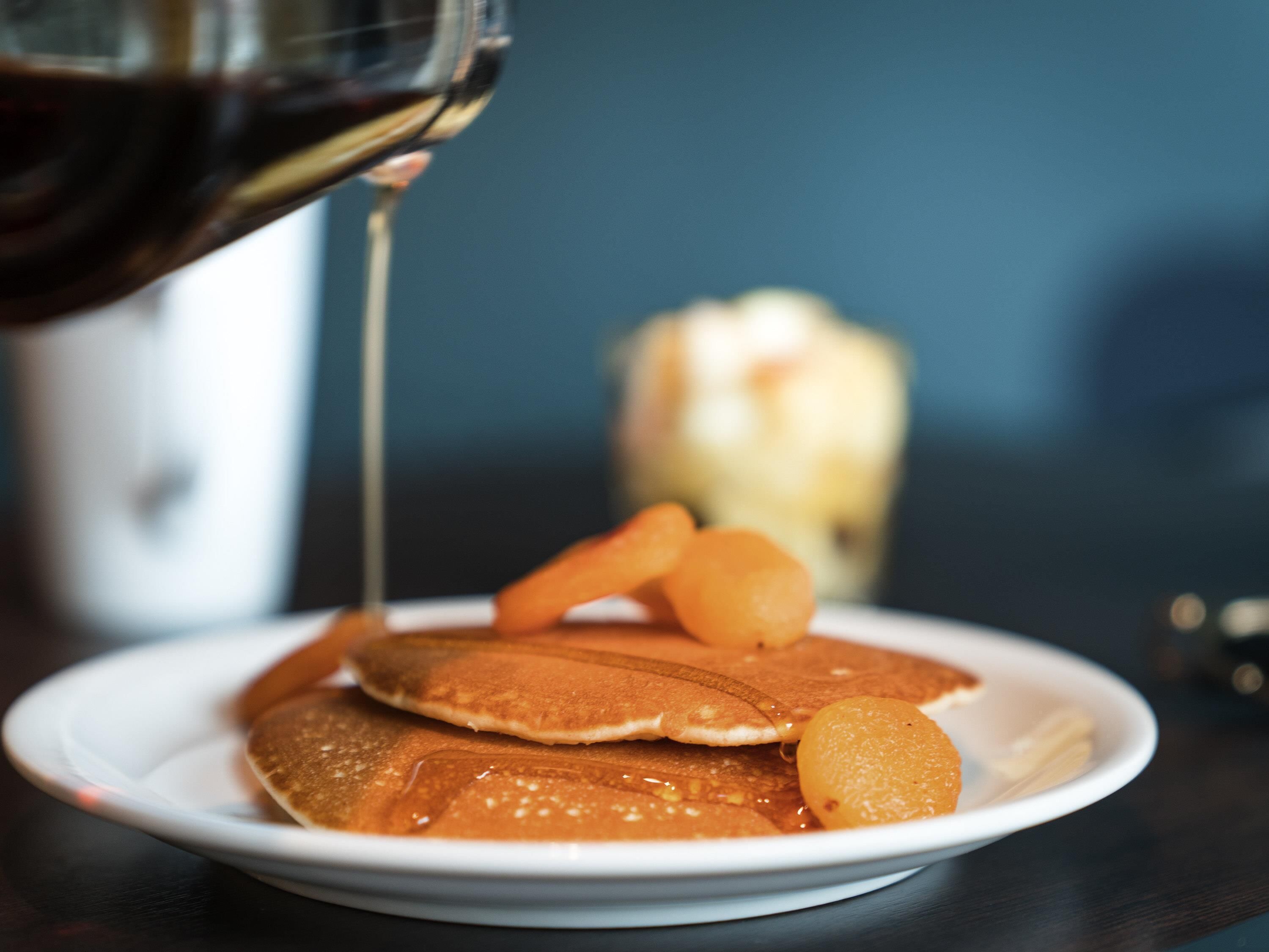 A plate of pancakes with syrup and a glass of a dark liquid, possibly coffee or tea, on a table.