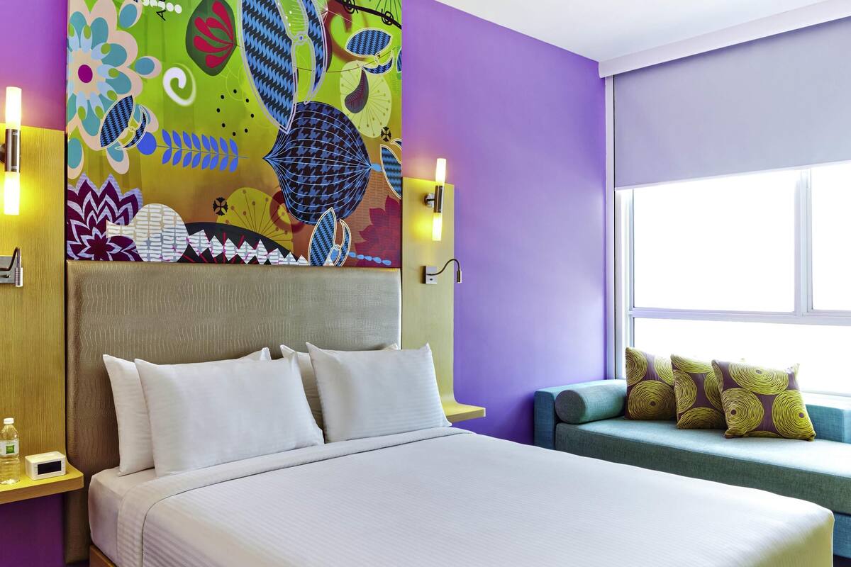 Una habitación de hotel con cama, sofá, un mural de colores y una ventana.