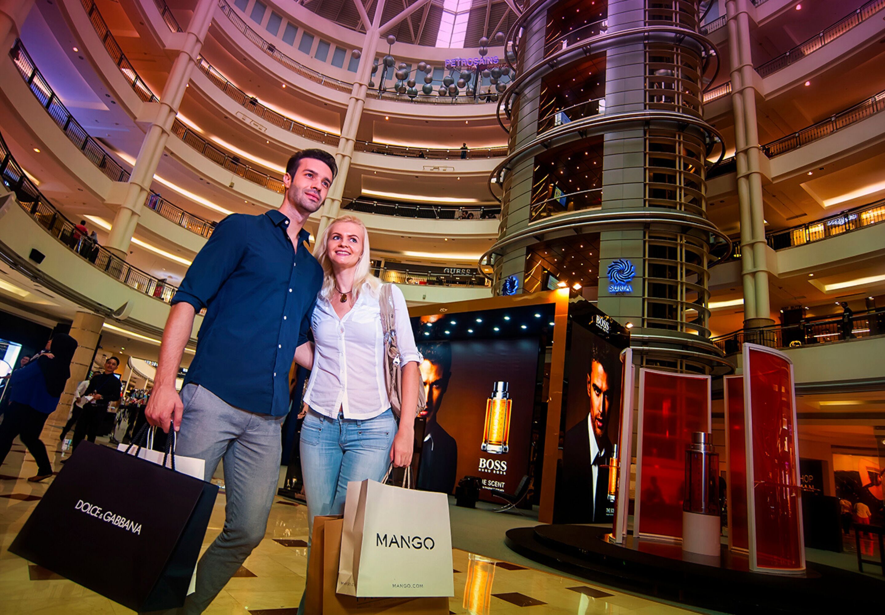 A multi-level shopping mall with a central atrium, escalators, and various retail stores.