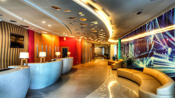 Un moderno vestíbulo de hotel con un mostrador de recepción curvo, zona de estar y una gran exhibición de arte digital en la pared.