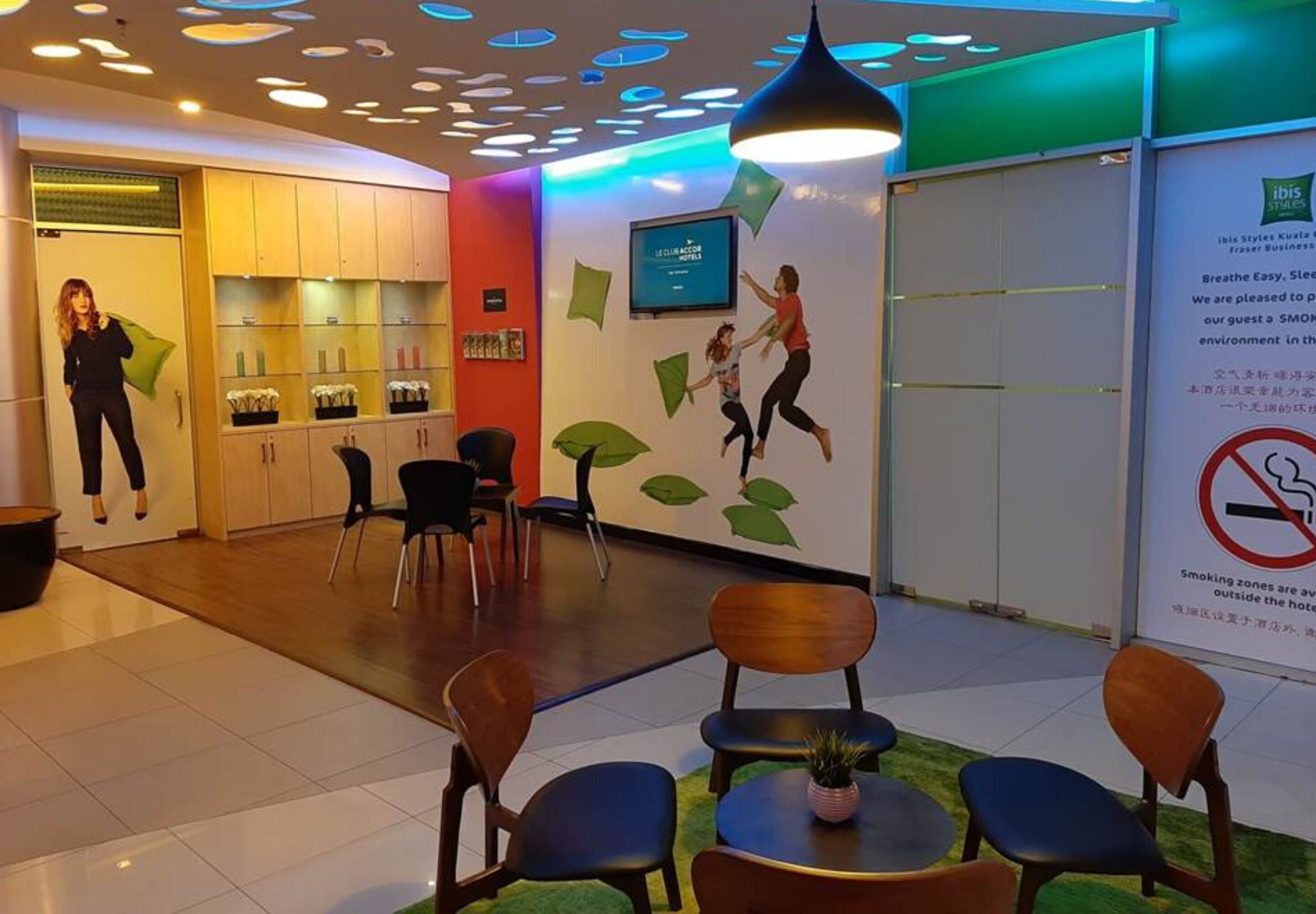 Eine Hotelhalle mit Empfangstresen, Sitzgelegenheiten und einer Wand mit einem digitalen Bildschirm, der eine Willkommensbotschaft zeigt.