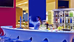 Una zona de bar con taburetes, una barra y una estantería con botellas.
