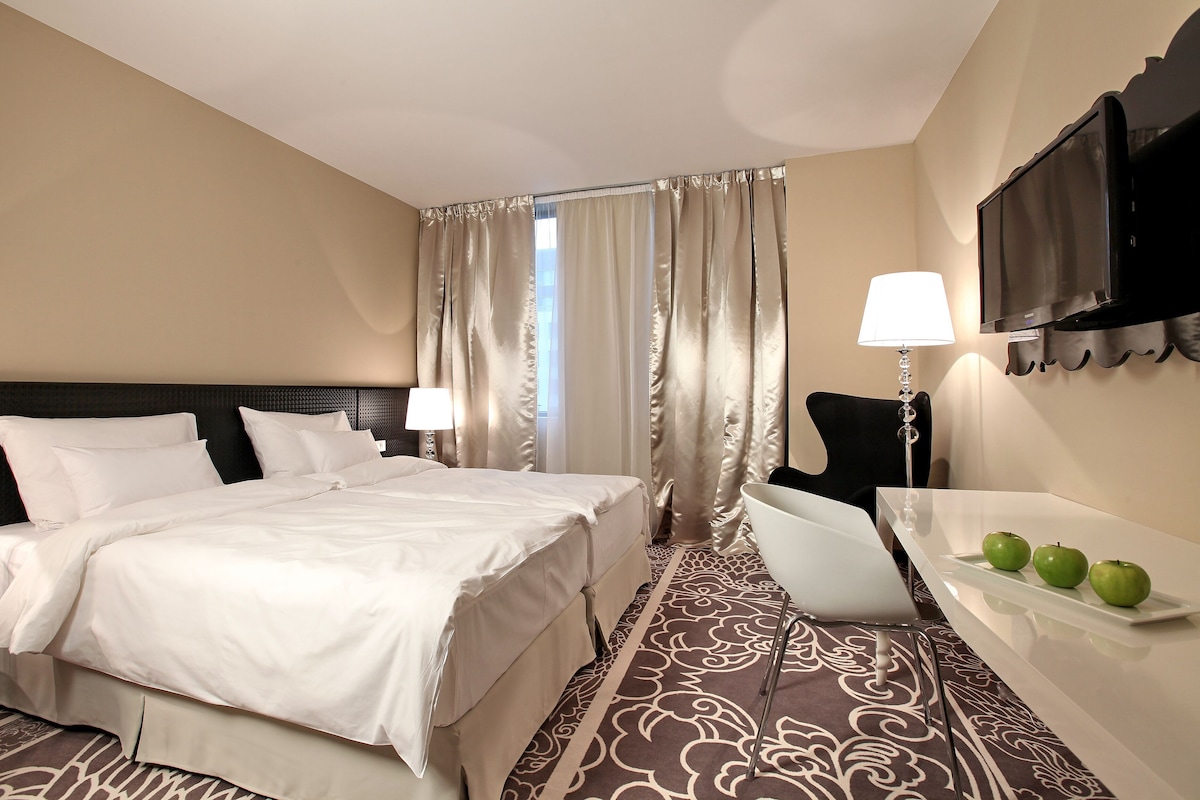 Una habitación de hotel con cama, escritorio con lámpara, televisión y ventana con cortinas.