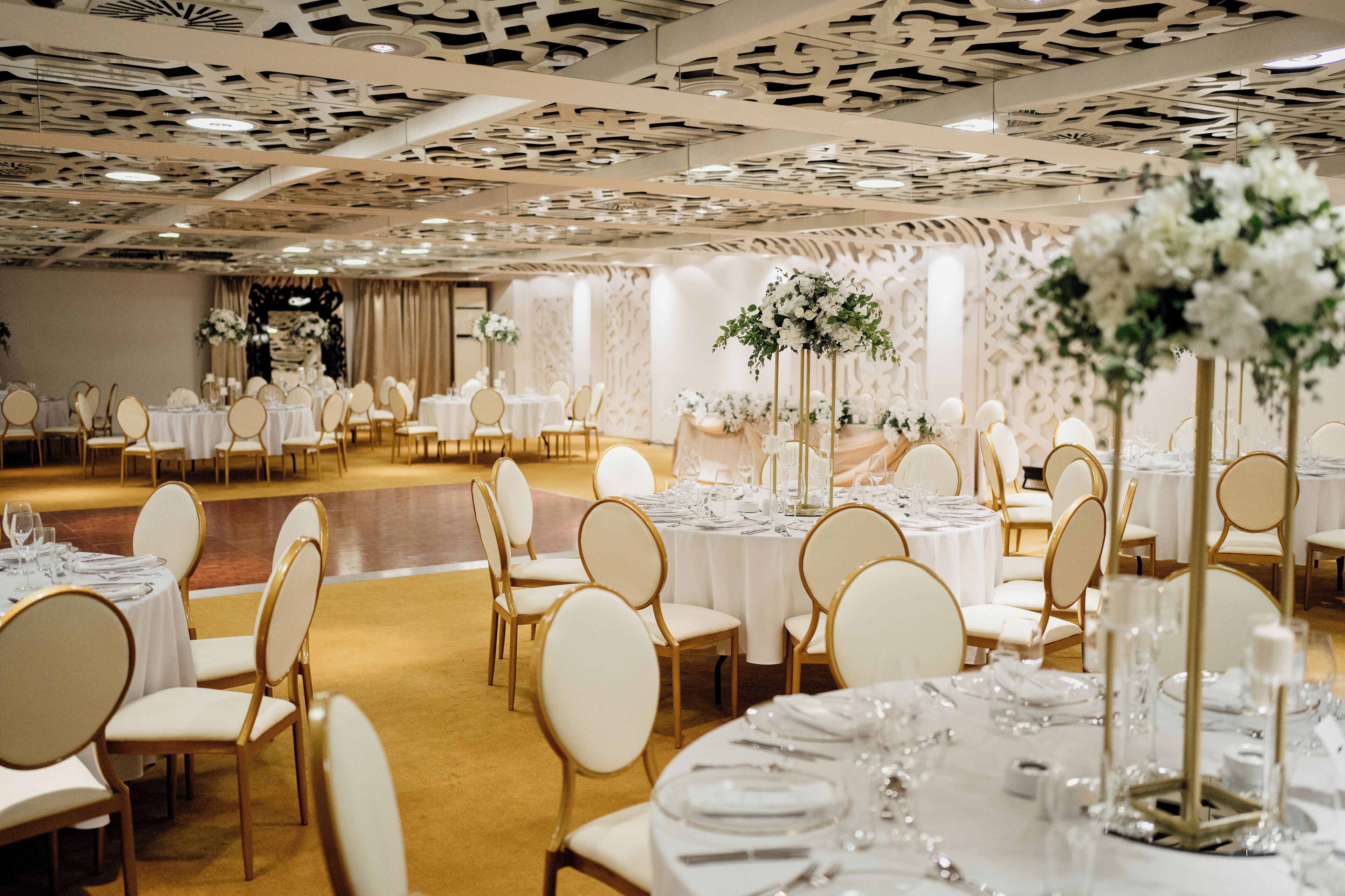 A banquet hall with round tables, white chairs, and floral centerpieces.