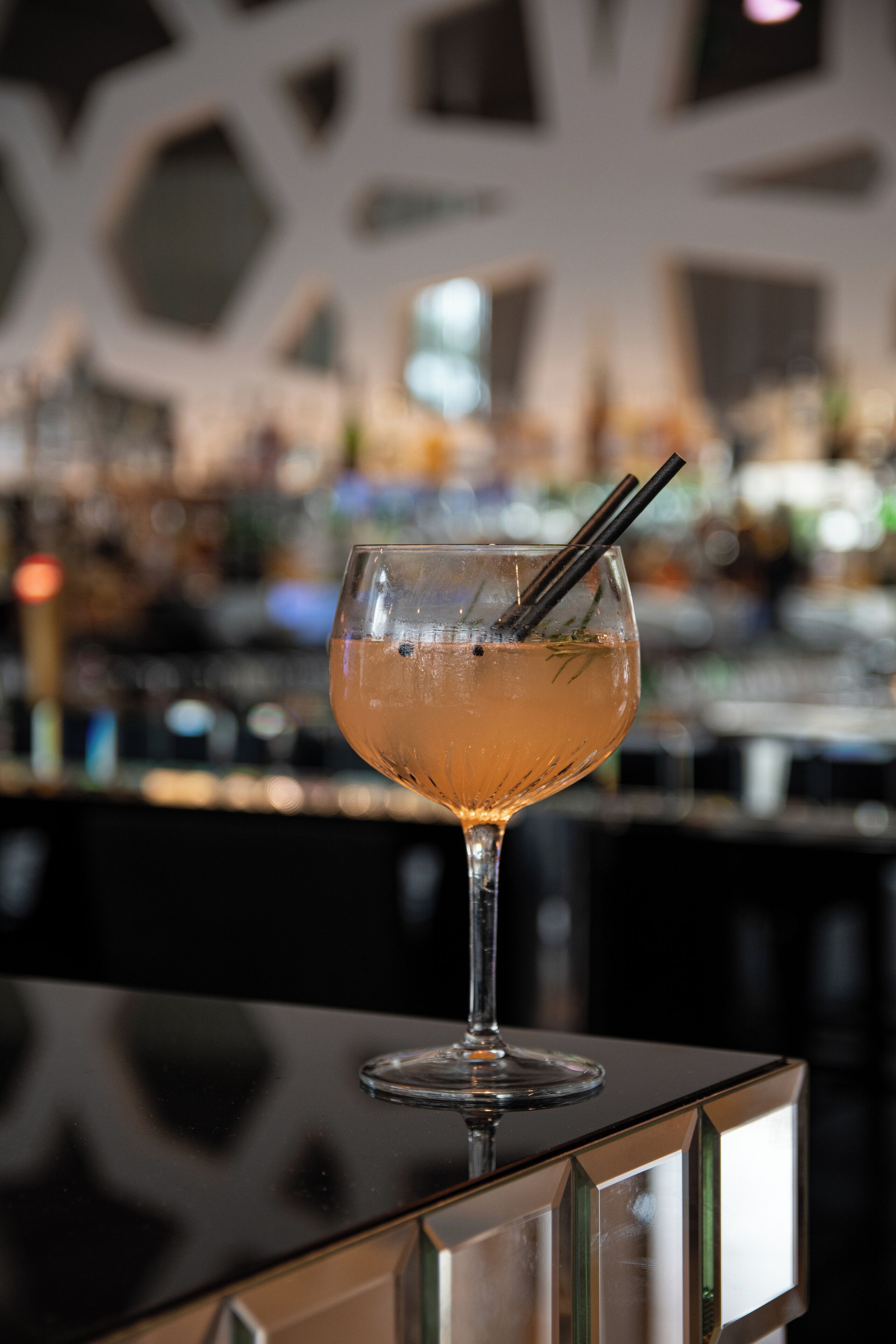 Een cocktailglas met een rietje op een reflecterend oppervlak.
