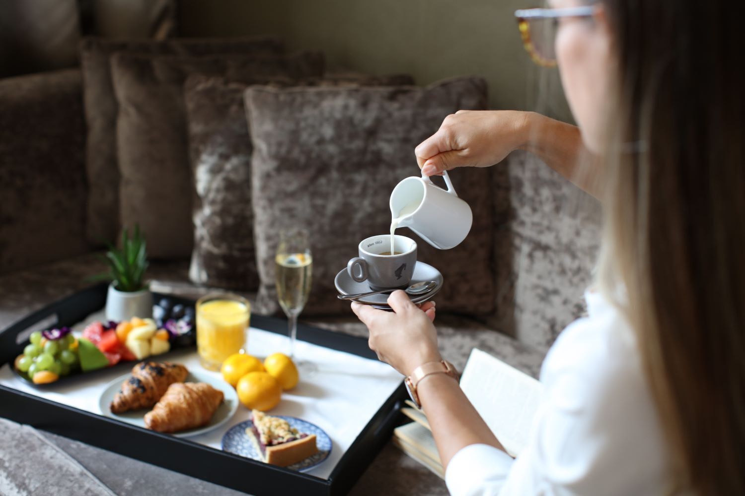 Ein Tablett mit Croissants, Obst, Saft und einer Kaffeetasse, aus der Kaffee gegossen wird.