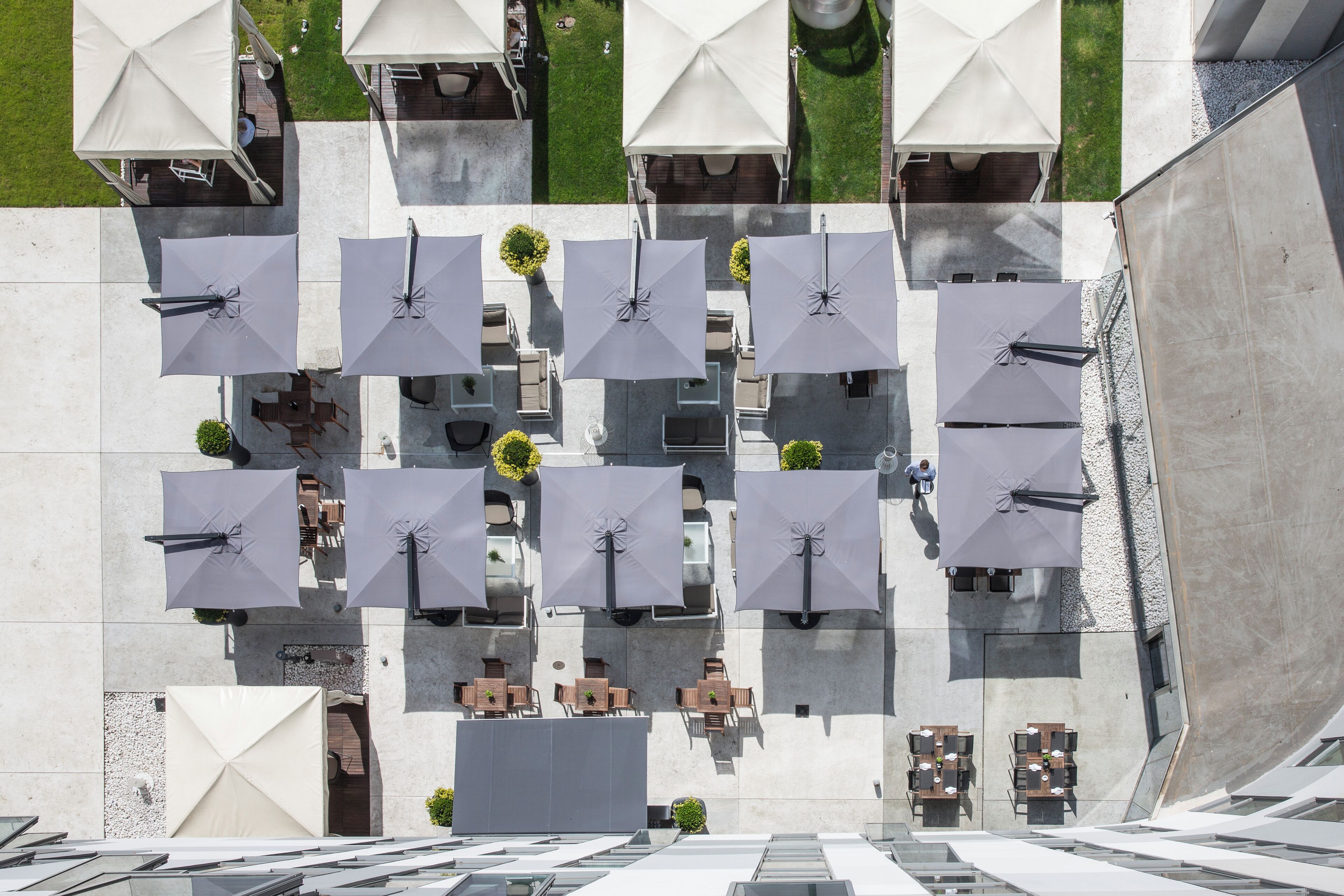 Vue aérienne d’une terrasse sur le toit, dotée de plusieurs tables et parasols, et entourée d’une structure en béton.