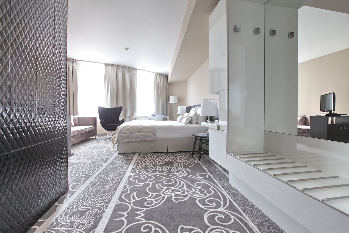 Habitación de hotel moderna con cama, zona de estar, escritorio, televisor y escalera.