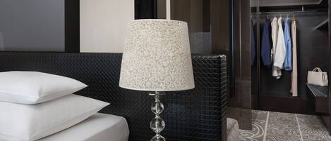 A modern hotel room with a bed, a bedside table with a lamp, a small table with a book, and a patterned rug.