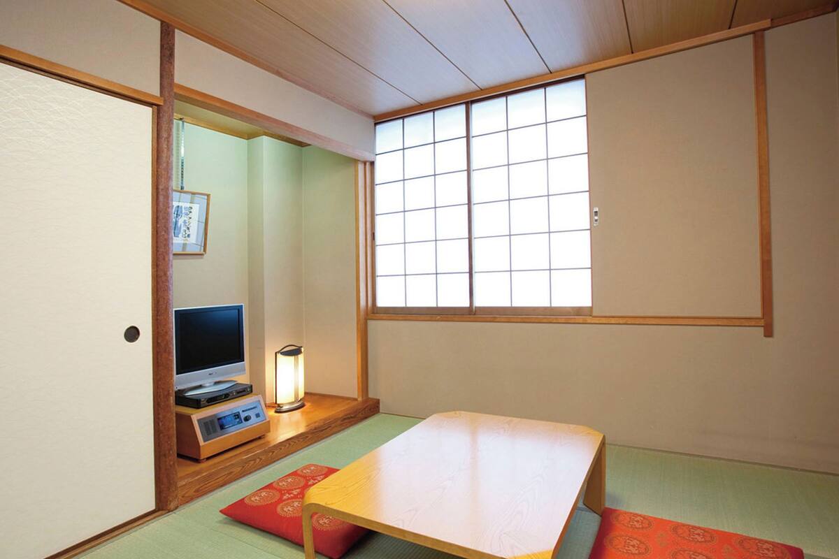A traditional Japanese room with tatami flooring, a low table, a television, and a window with grid panes.