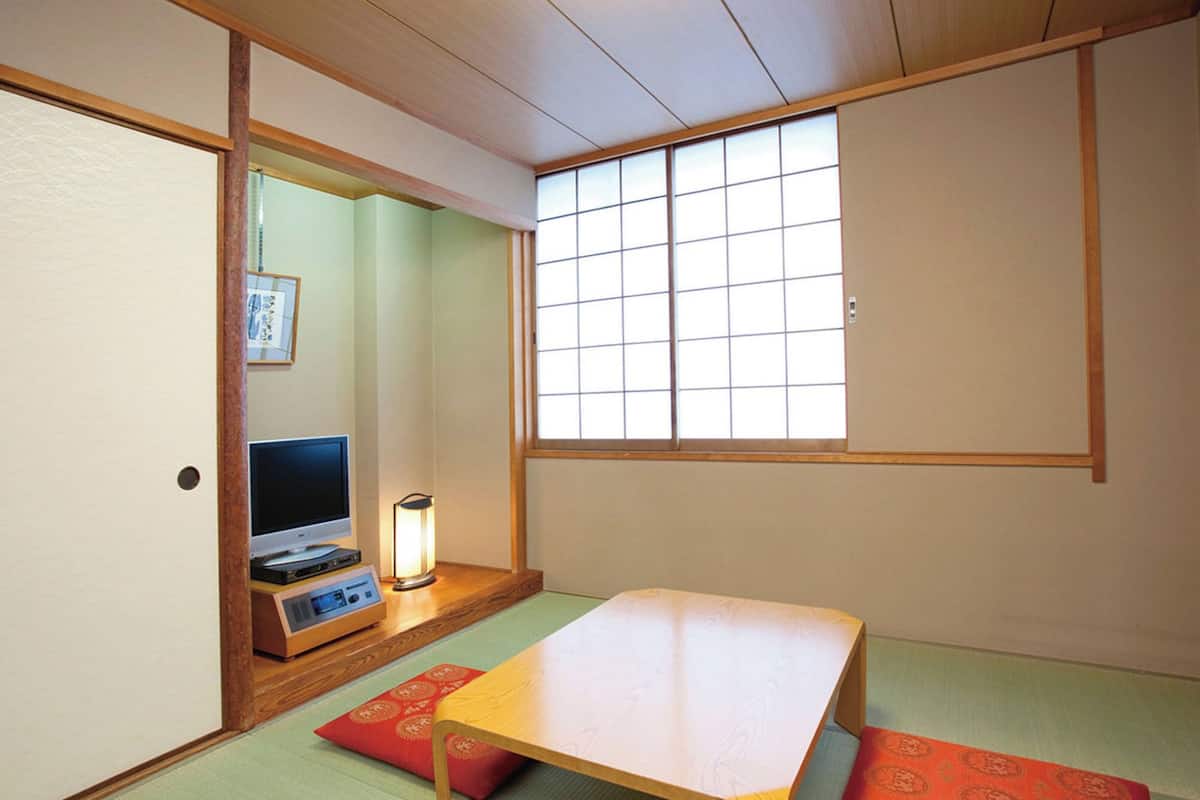 Una habitación japonesa tradicional con suelo de tatami, una mesita baja, un televisor y una ventana con celosías.