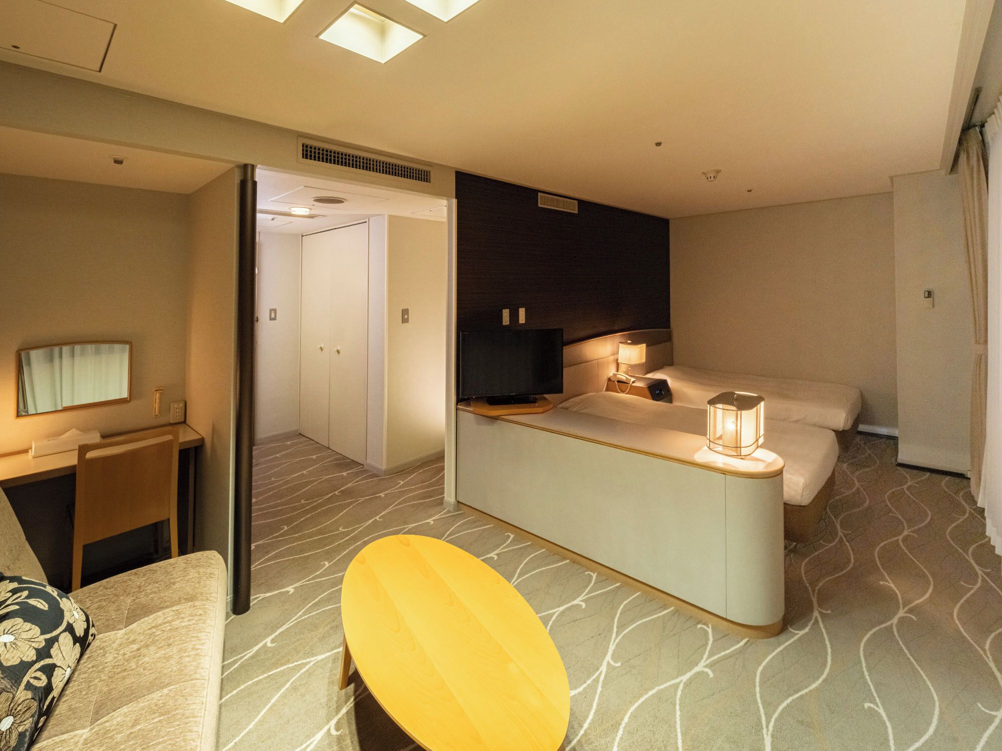 A hotel room with a bed, bedside table, lamp, and a small seating area.