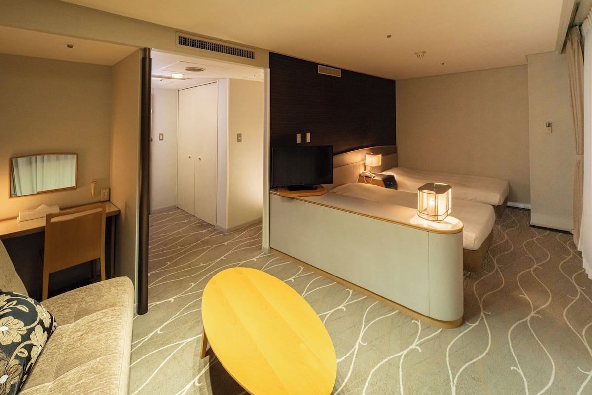 A hotel room with a bed, bedside table, lamp, and a small seating area.