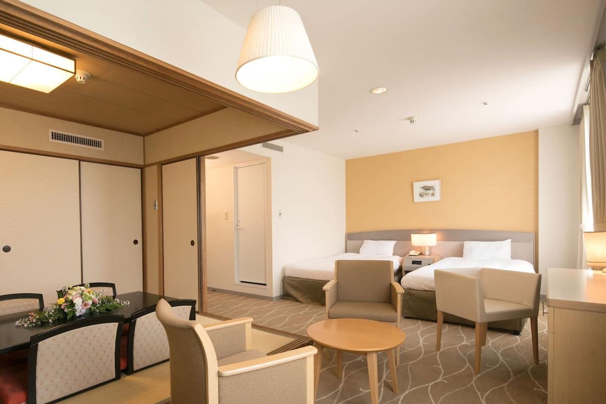 A hotel room with a dining area, two beds, a small table, and a sofa.