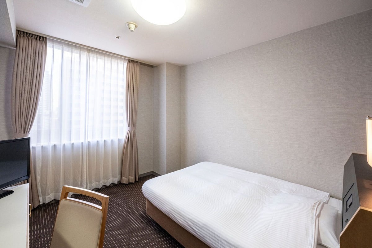 A hotel room with a bed, a desk, a chair, and a window with curtains.