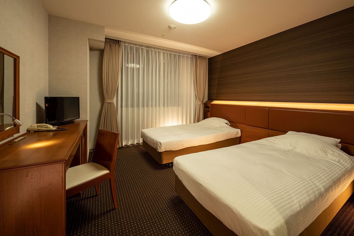 A hotel room with two beds, a desk with a telephone, a chair, and a television.