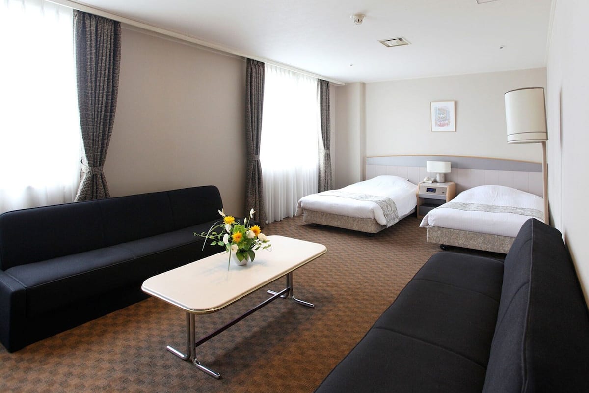 A hotel room with a sofa, a bed, a bedside table, and a small table with a vase of flowers.