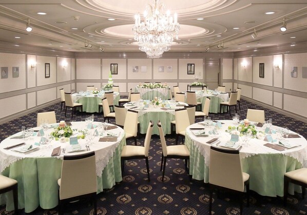 Un salón de banquetes con mesas redondas, cada una cubierta con manteles blancos y sillas, y una araña colgando del techo.