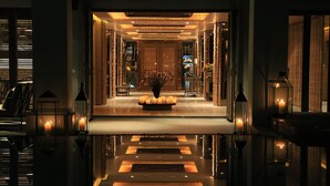 Un lobby de hotel lujoso con piso reflectante, un arreglo floral central y una puerta de madera tradicional.