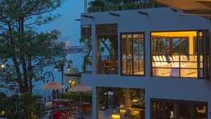 Un edificio moderno con zona de comedor con vistas a un cuerpo de agua, con amplios ventanales y mesas al aire libre.
