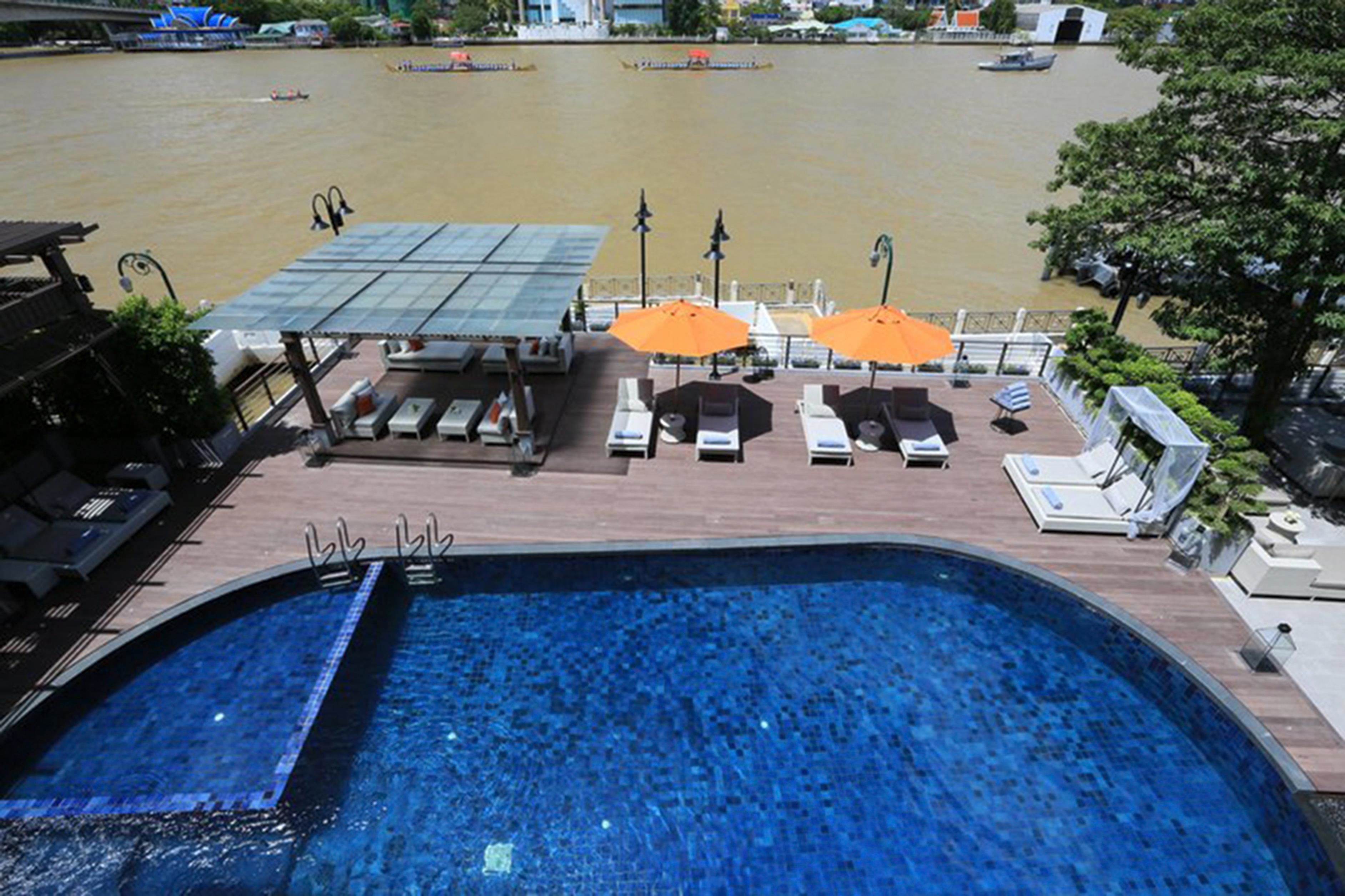 A swimming pool with lounge chairs and umbrellas, overlooking a river with boats.
