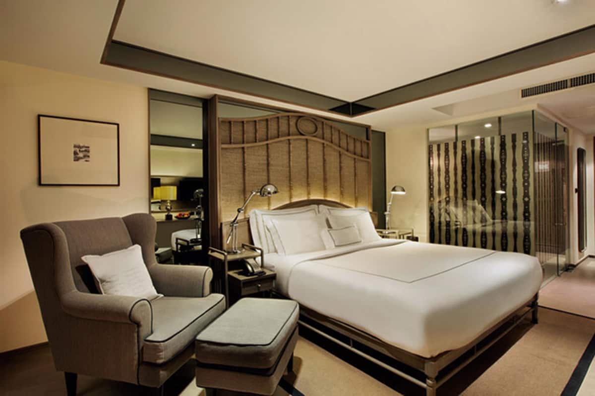 A modern hotel room with a large bed, a sofa, a nightstand, and a glass partition.