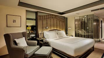 A modern hotel room with a large bed, a sofa, a nightstand, and a glass partition.
