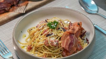 Um prato de espaguete com bacon e um enfeite, acompanhado de uma pequena tigela de molho e um pedaço de pão sobre uma mesa.