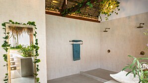 A bathroom with a large mirror surrounded by greenery, a towel rack, and a white sink.