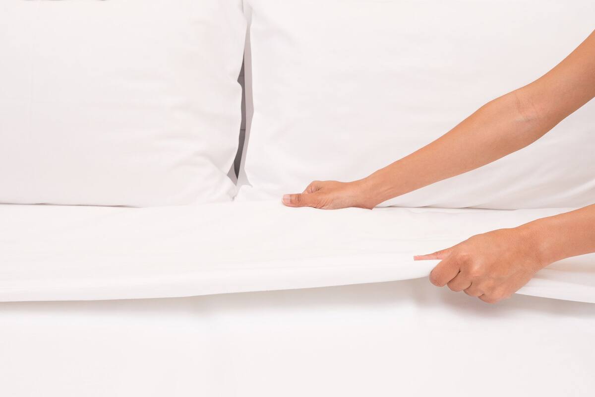 A person adjusting a white mattress on a bed.