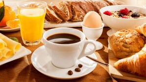 A breakfast setting with a cup of coffee, orange juice, croissants, a bowl of cereal with berries, and a plate of cheese.