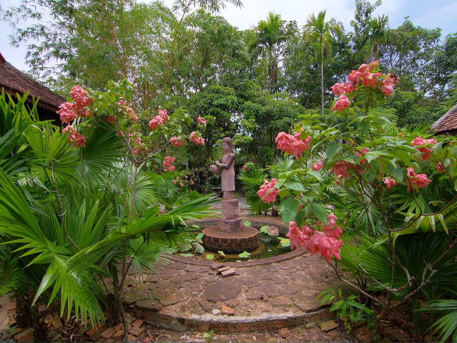 Un jardín con una estatua central, rodeado de exuberante vegetación y plantas florecientes.