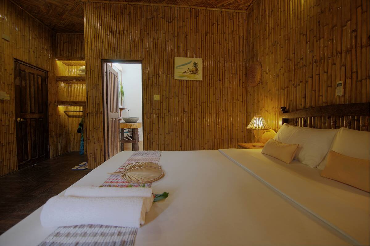 A room with a large bed, a wooden wall, a small table with a lamp, and a picture on the wall.